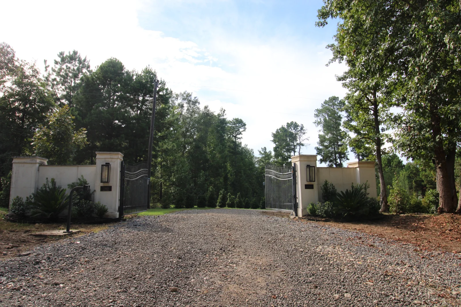 Gravel entrance between pale masonry gate pillars surrounded by trees